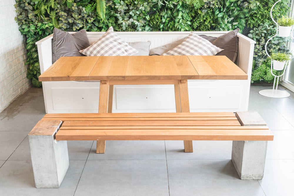 Un set de muebles multifuncionales para exteriores, compuesto por una mesa y un banco de madera con detalles en concreto, acompañado de un sofá con cojines. Perfecto para optimizar espacios en jardines y terrazas con estilo y funcionalidad.
